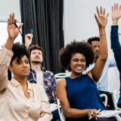Group of young people sitting on conference together. Group of young people sitting on conference together while raising their hands to ask a question. Business team meeting seminar training concept.